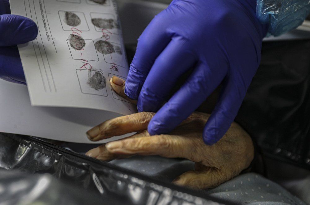 An employee takes the fingerprints of a woman who died from the new coronavirus before her remains are cremated at La Recoleta crematorium in Santiago, Chile, Saturday, June 27, 2020. (AP Photo/Esteban Felix)
